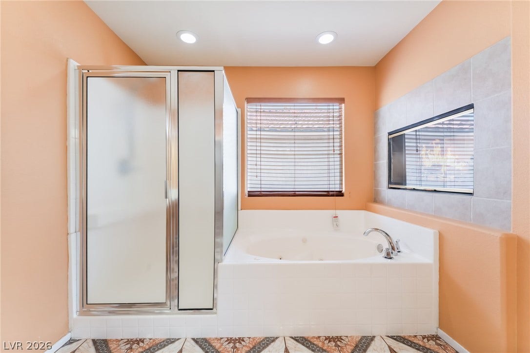 A spacious soaking tub sits adjacent to a glass shower enclosure with decorative tiled flooring.