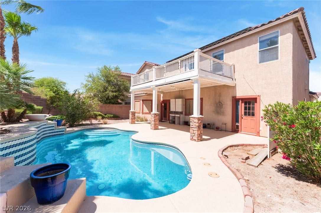 An inviting backyard oasis features a shimmering pool alongside a covered patio and upper-level balcony.