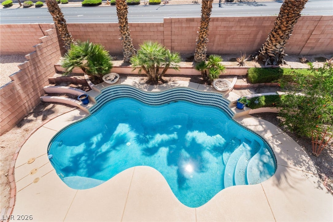 An inviting in-ground pool is framed by towering palm trees and secure block fencing.