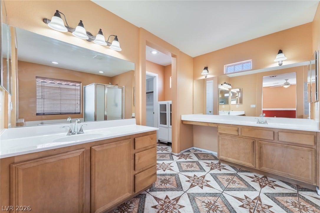 Ornate tiled flooring anchors a spacious master bathroom featuring dual wood vanities and ample mirror glass.