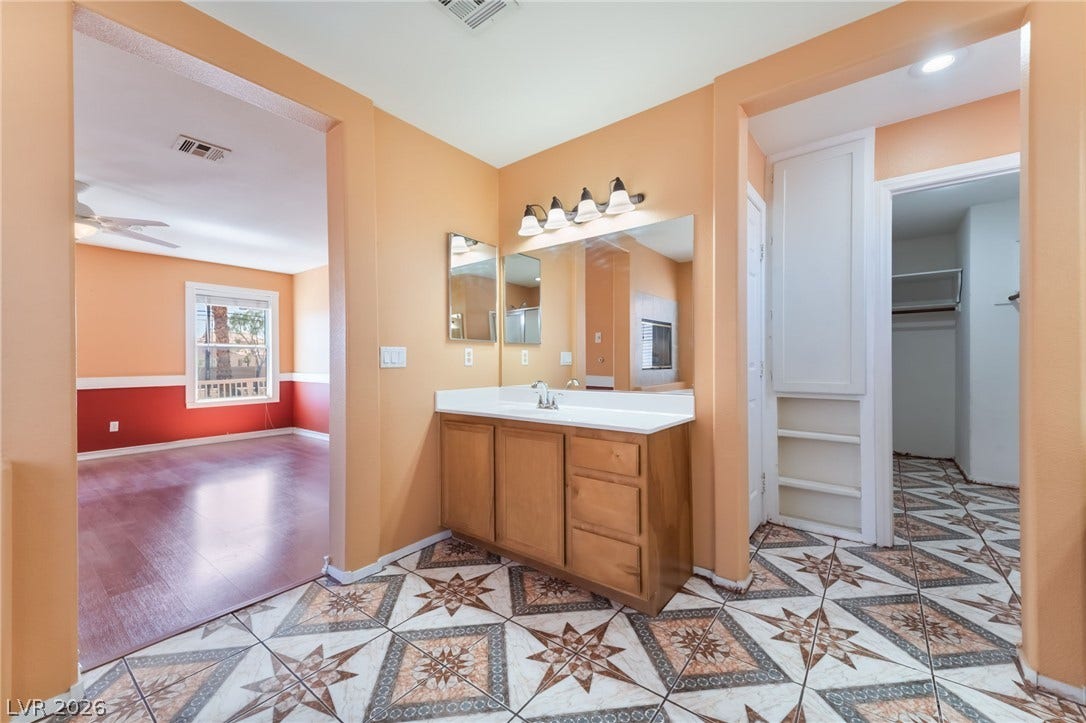 Distinctive patterned tile floors anchor this master bathroom featuring a wooden vanity and built-in shelving.