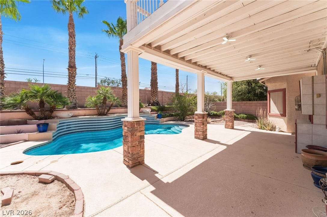 Shaded concrete decking borders a sparkling in-ground pool surrounded by towering palm trees.