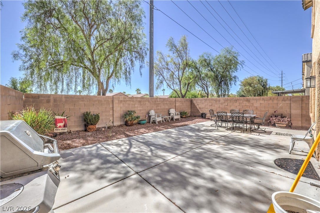 A spacious concrete patio is enclosed by a privacy wall and shaded by mature trees.