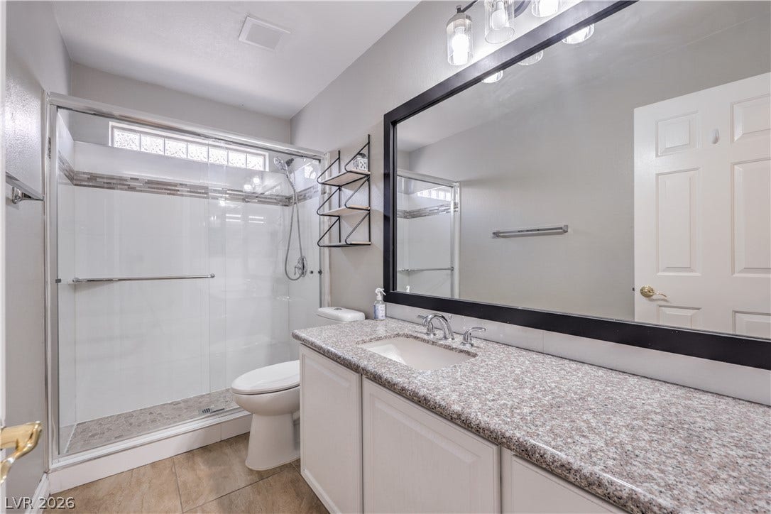A modern vanity with stone counters anchors this cleanly designed bathroom featuring a walk-in shower.