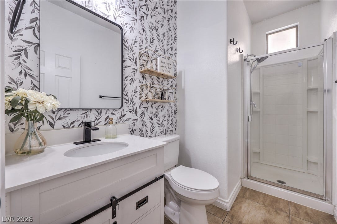A glass-enclosed walk-in shower pairs with a single vanity and tile flooring.
