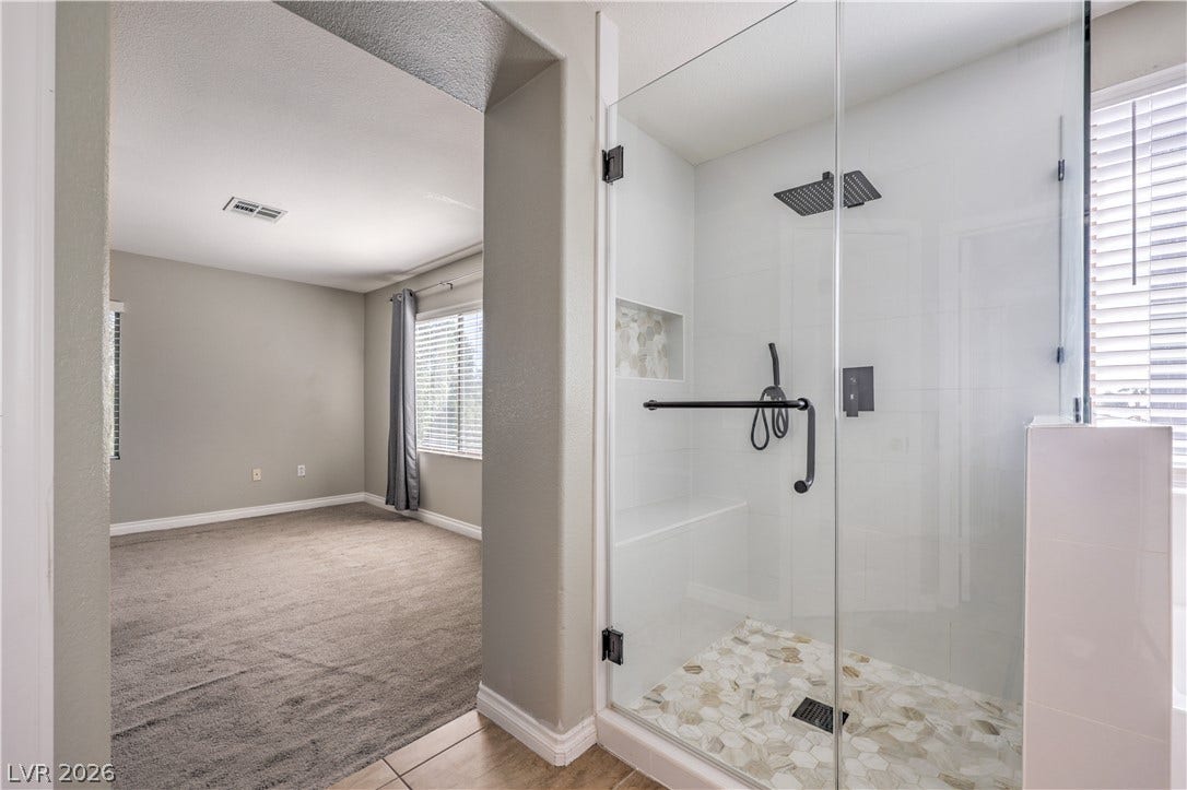 A glass-enclosed walk-in shower sits adjacent to a carpeted bedroom suite.