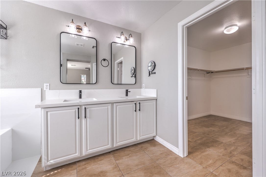 A dual vanity with stone counters connects seamlessly to a spacious walk-in closet.