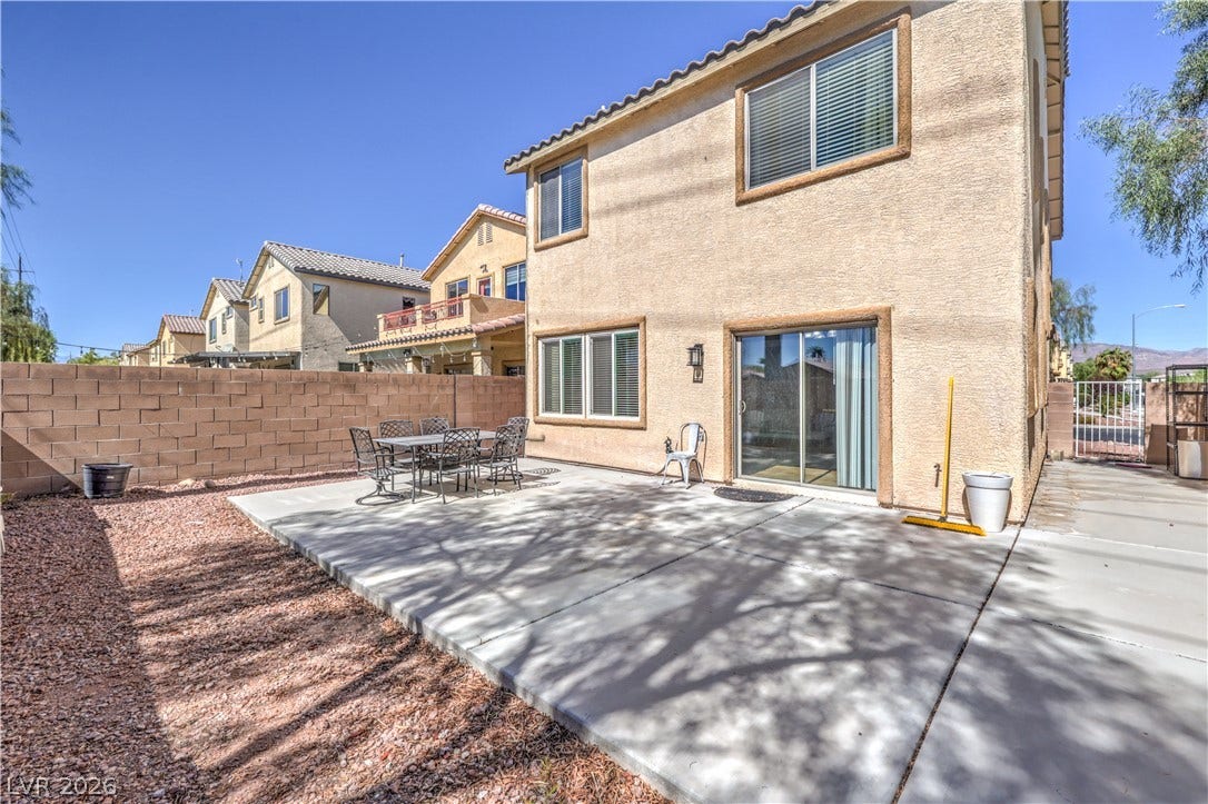 An open concrete patio extends from the stucco exterior under clear blue skies.