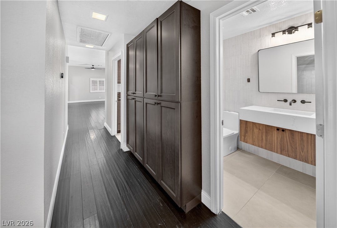1740 Bluffs Drive, Henderson, NV 89014 Rich wood floors sweep through the hallway past custom cabinetry into a modern bathroom.