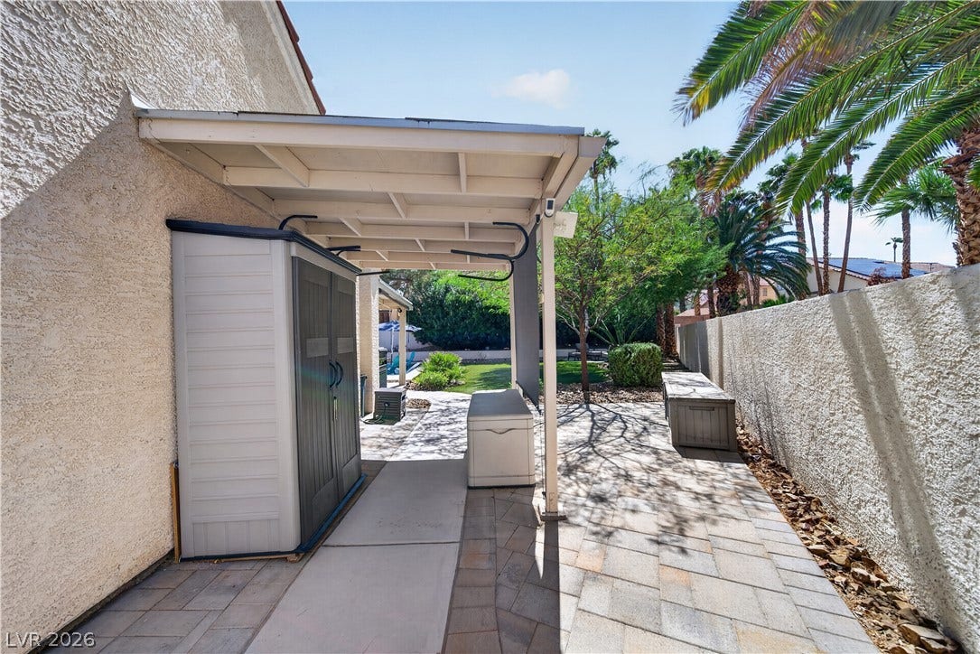 1740 Bluffs Drive, Henderson, NV 89014 A covered concrete patio leads into the fenced backyard bordered by towering palms.