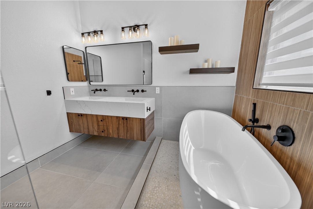 1740 Bluffs Drive, Henderson, NV 89014 A contemporary bathroom features a floating vanity, tiled floors, and a deep soaking tub.