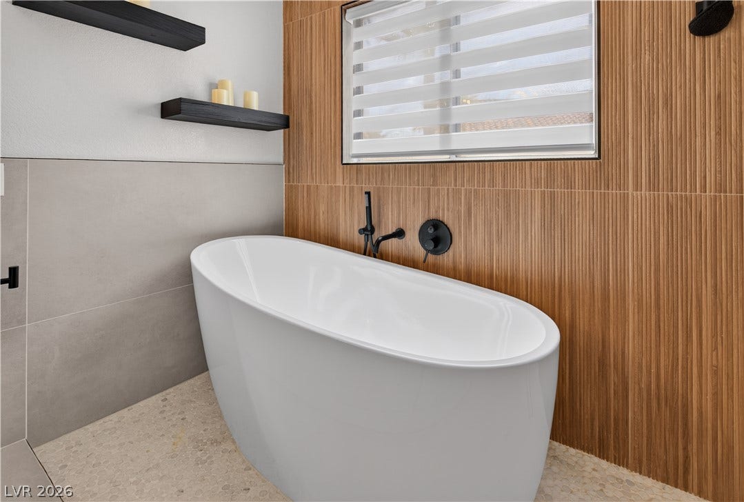 1740 Bluffs Drive, Henderson, NV 89014 Modern vertical wood paneling frames a deep soaking tub beneath a light-filtering window.