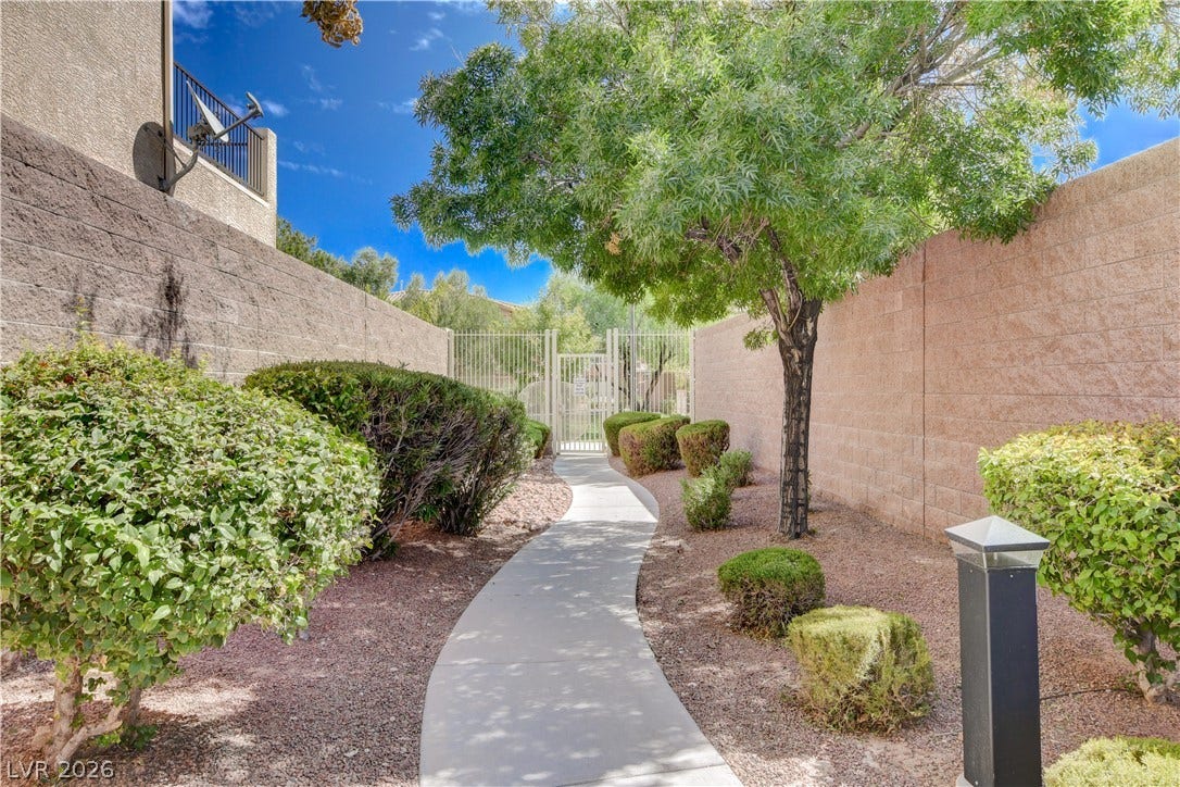 4120 Hawks Glide Avenue, North Las Vegas, NV 89084 A curved concrete pathway winds through landscaped grounds enclosed by high block walls.