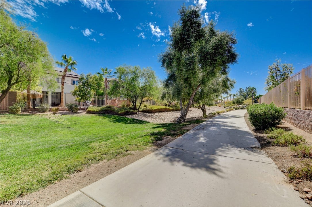 4120 Hawks Glide Avenue, North Las Vegas, NV 89084 A paved community pathway winds past manicured lawns, mature trees, and a secure perimeter fence.