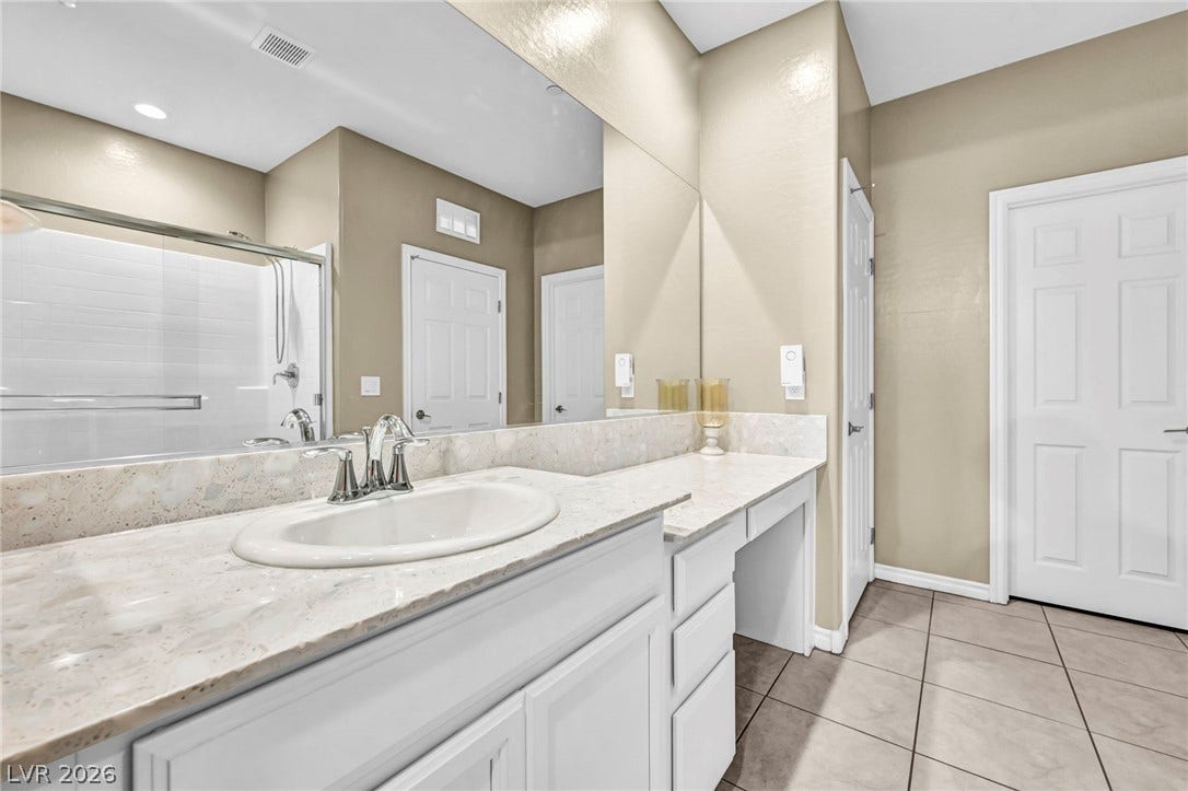 Polished stone countertops and clean tile flooring define this spacious bathroom vanity area.