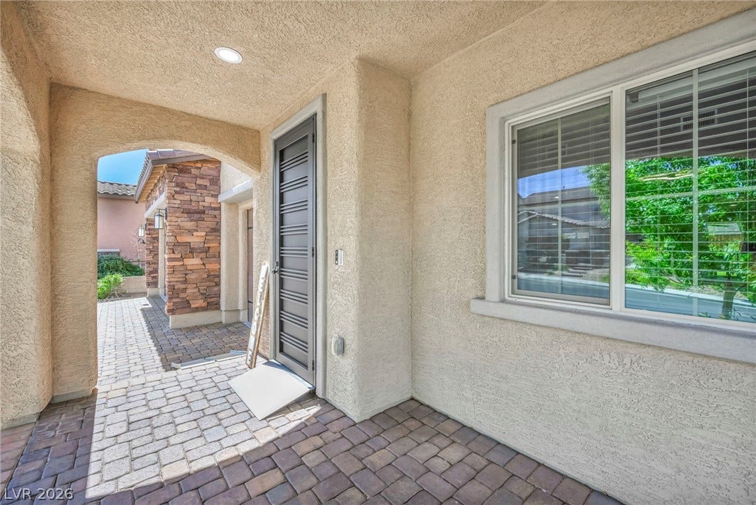 An inviting covered entryway features robust stucco pillars, stone accents, and classic paver flooring.