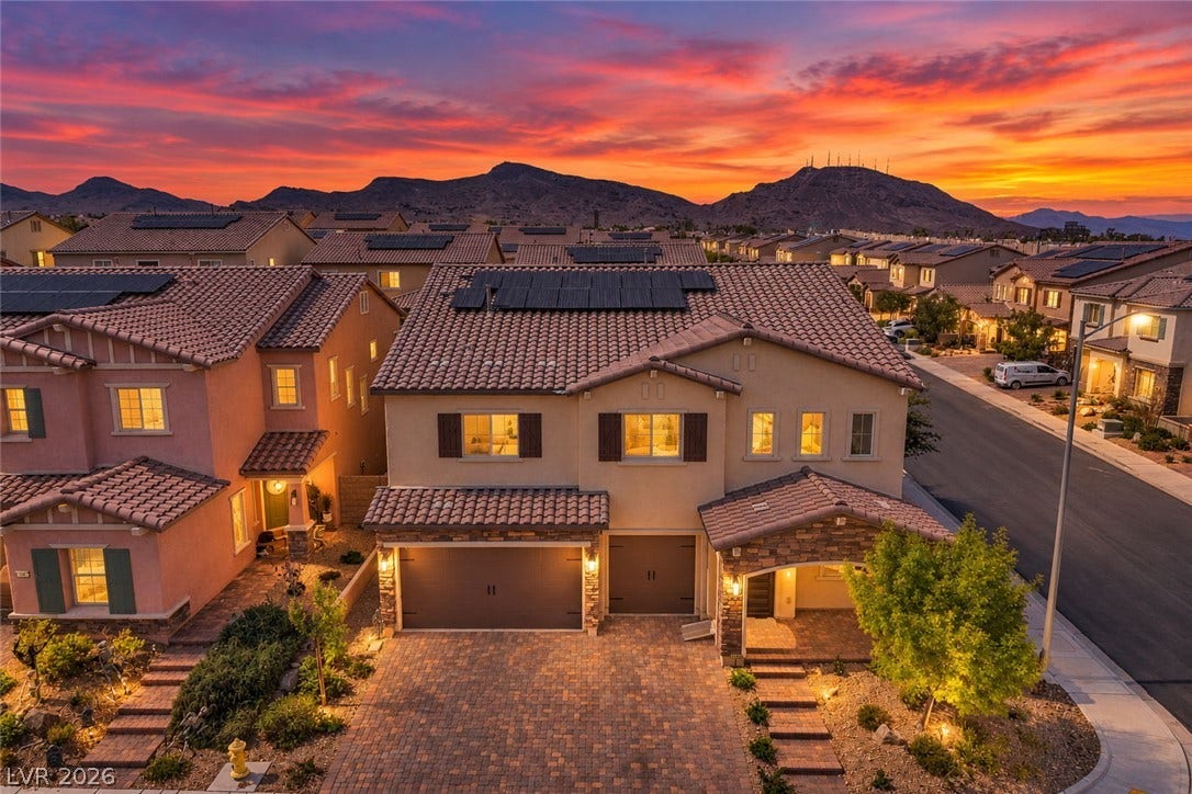 Dramatic mountain backdrops frame this modern multi-level home featuring solar panels and a paved driveway.