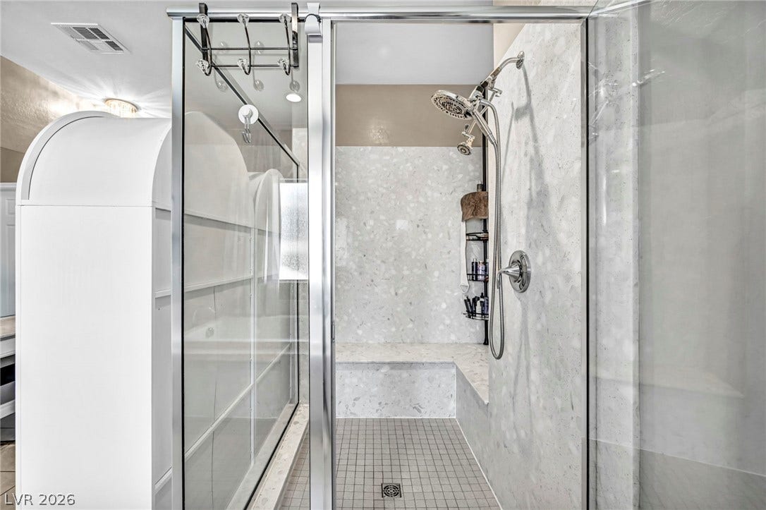 Polished stone tiling and a built-in bench highlight this modern walk-in shower enclosure.
