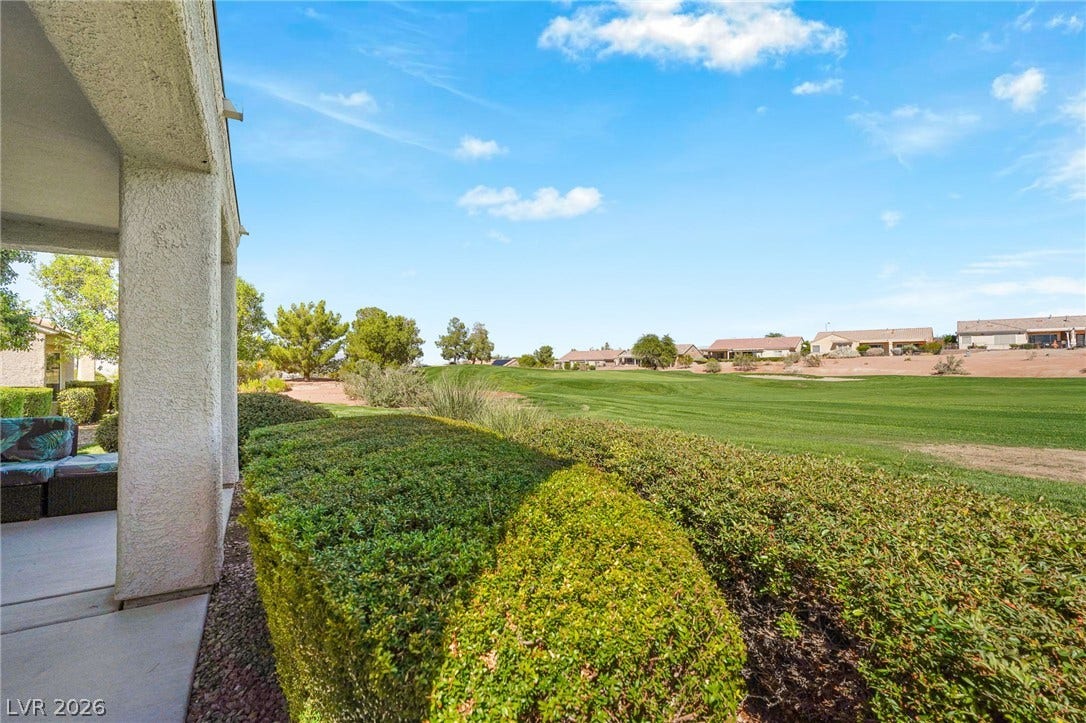 2738 Grand Forks Road, Henderson, NV 89052 Manicured hedges frame a covered patio opening directly onto a lush green fairway under sunny skies.