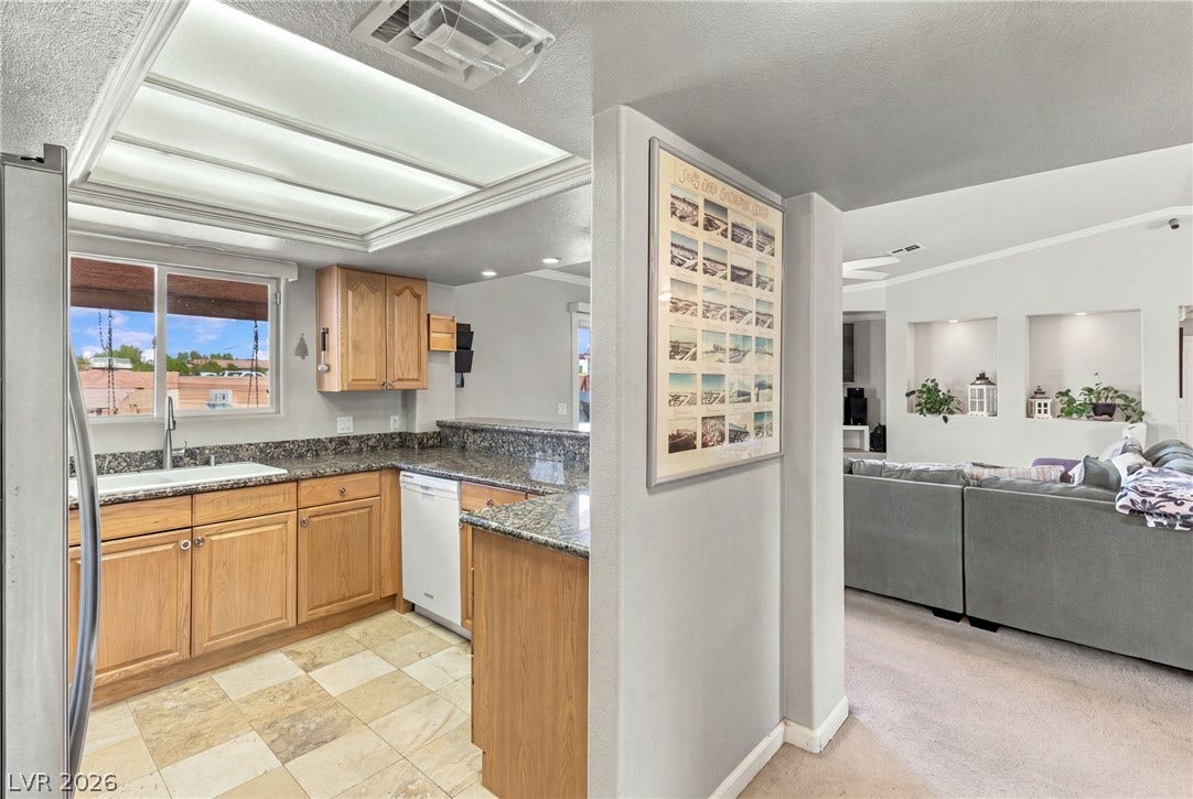 6560 Whispering Sands Drive, Las Vegas, NV 89131 An open floorplan seamlessly connects the stone-countertop kitchen to the adjacent carpeted living area.