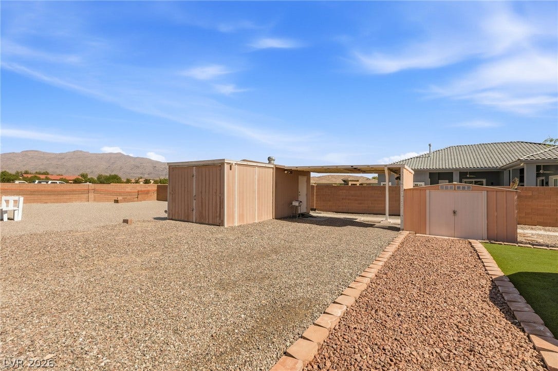 6560 Whispering Sands Drive, Las Vegas, NV 89131 A spacious gravel yard features multiple detached storage buildings set against mountain backdrops.