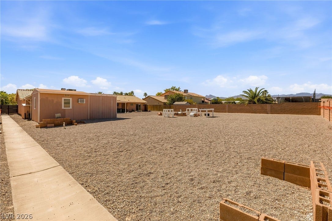 6560 Whispering Sands Drive, Las Vegas, NV 89131 A spacious gravel yard with a concrete walkway offers distant mountain views under blue skies.
