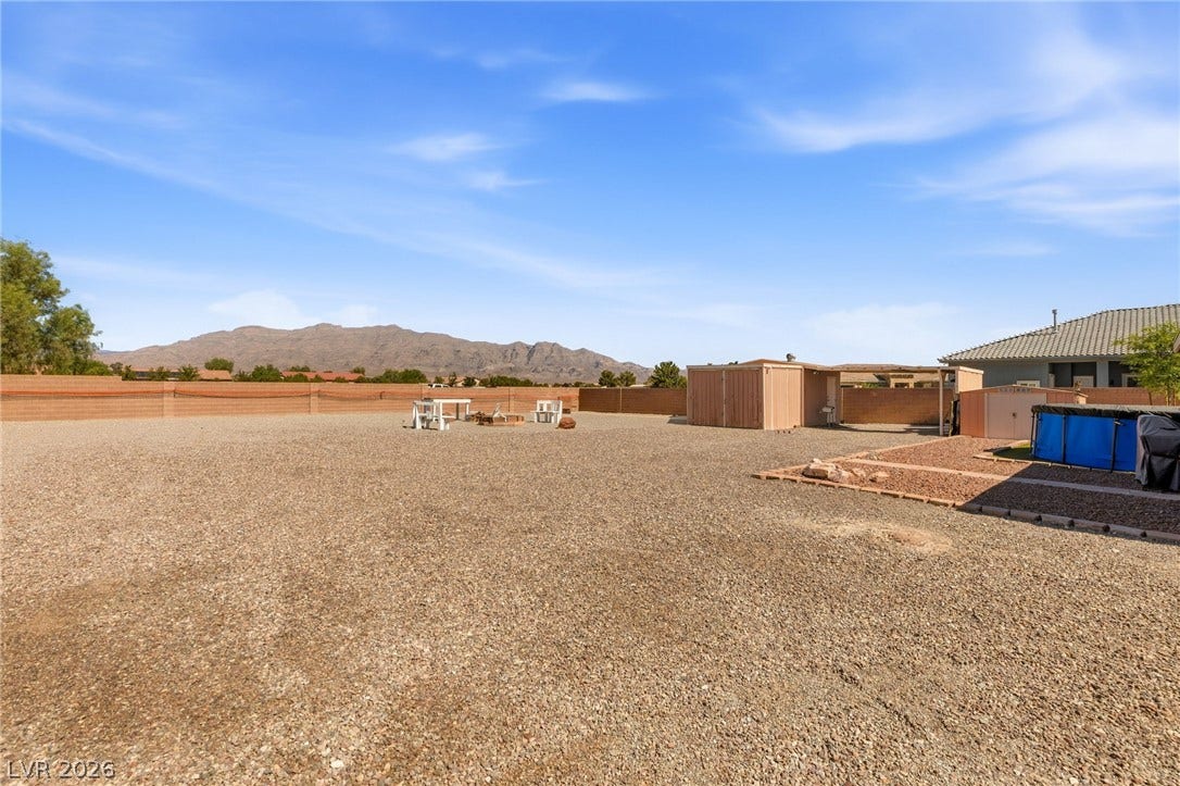 6560 Whispering Sands Drive, Las Vegas, NV 89131 An expansive gravel yard showcases outbuildings against a backdrop of distant mountains under blue skies.