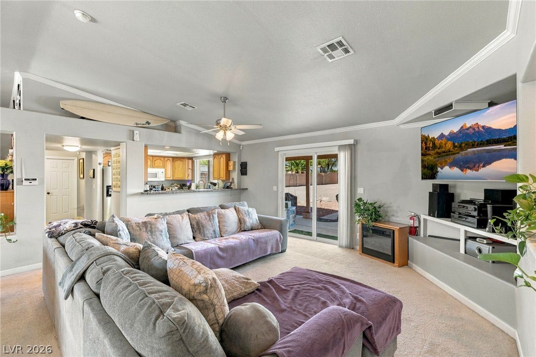 6560 Whispering Sands Drive, Las Vegas, NV 89131 An open floorplan living room features plush carpeting, crown molding, and sliding glass doors.