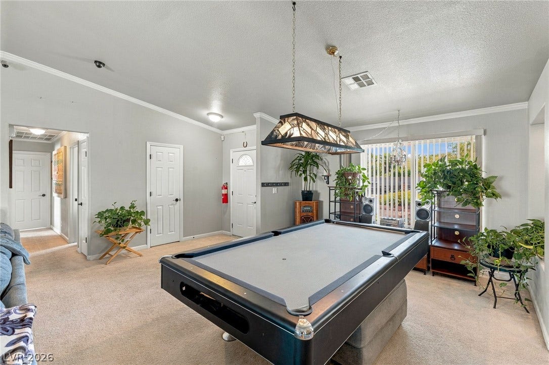6560 Whispering Sands Drive, Las Vegas, NV 89131 Crown molding and glass sliding doors frame a versatile game room with neutral carpeting.