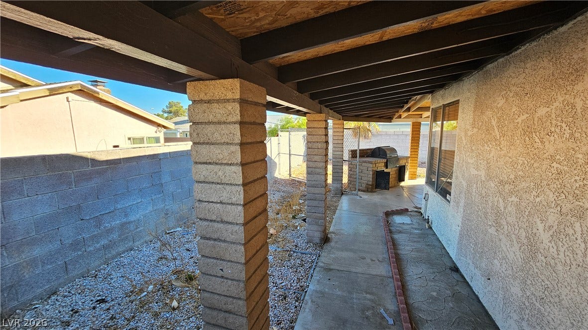 6777 Ledgewood Drive, Las Vegas, NV 89103 A sheltered concrete walkway runs alongside the stucco exterior beneath sturdy support pillars.
