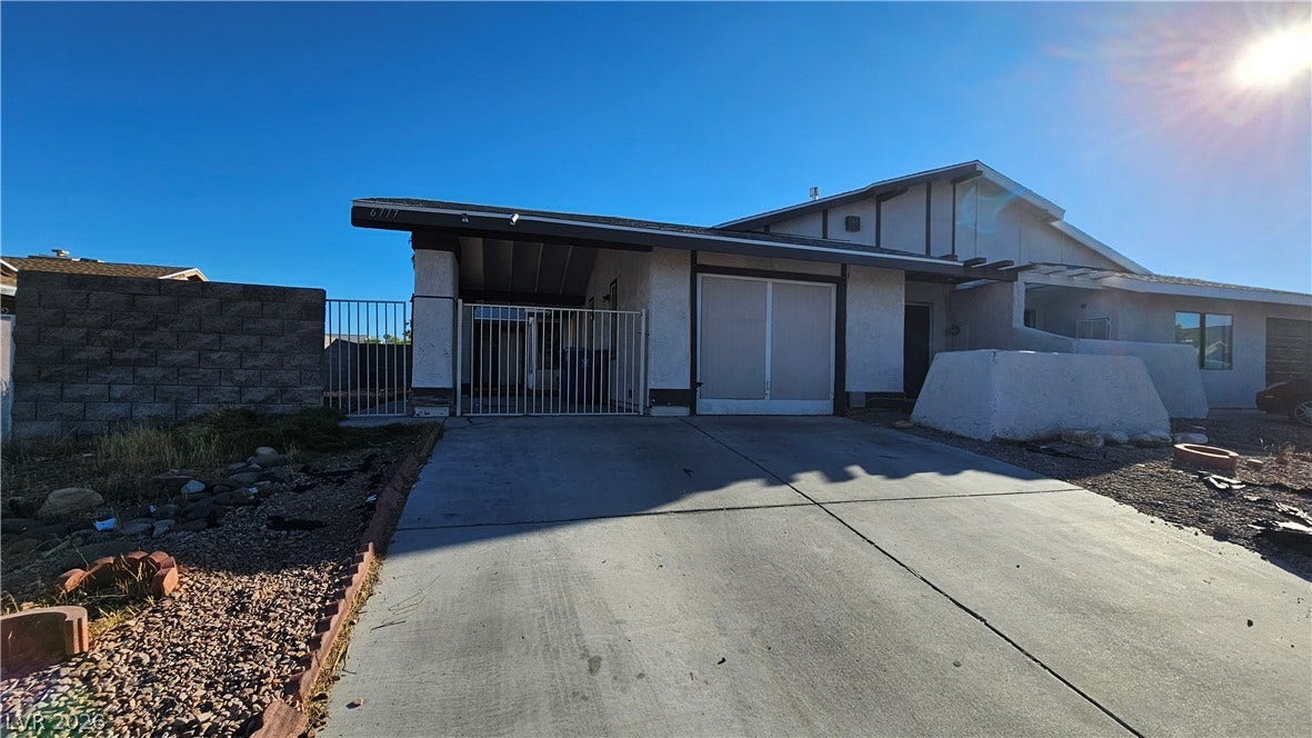 6777 Ledgewood Drive, Las Vegas, NV 89103 A spacious concrete driveway leads toward the gated carport and classic stucco facade.