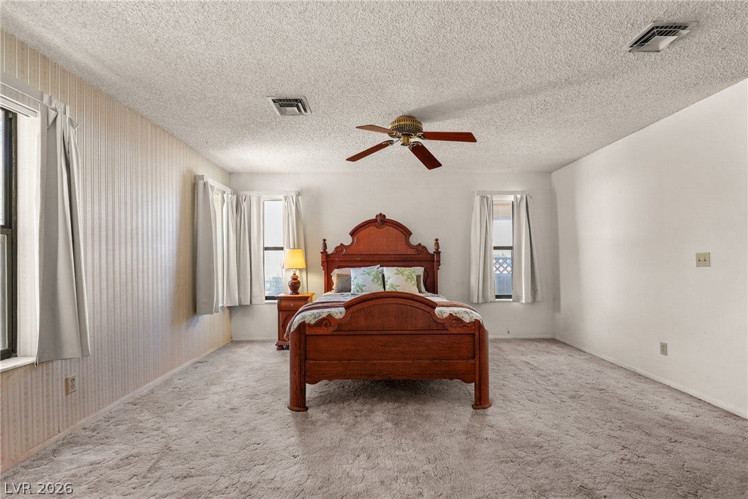 5601 Paseo Recallo Court, Las Vegas, NV 89108 Plentiful natural light fills a spacious bedroom lined with textured carpet flooring.