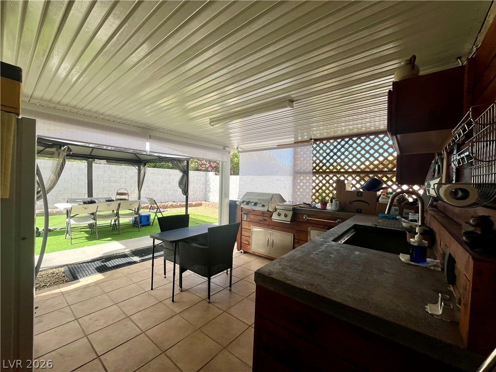 15 Rue des Champs, Henderson, NV 89074 An outdoor kitchen setup under a covered patio looks out to the fenced yard.
