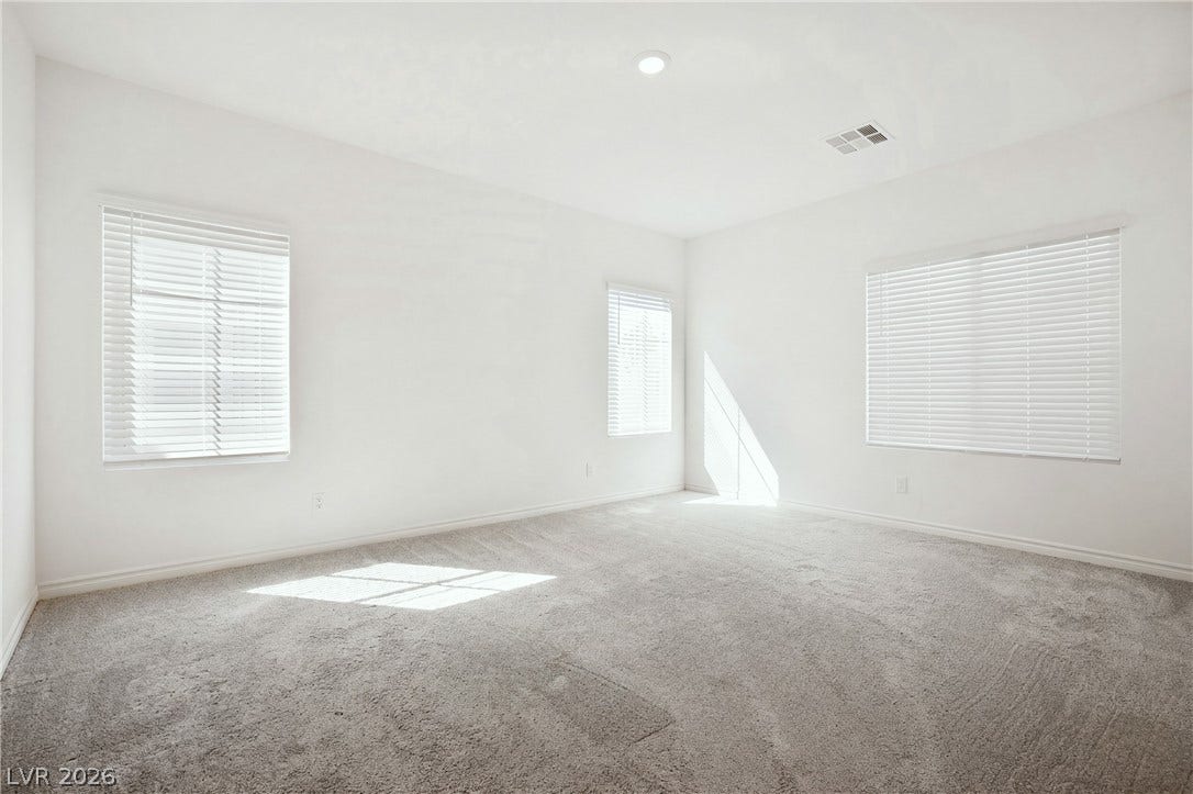 Plentiful natural light streams across carpeted flooring through multiple large windows in this versatile room.