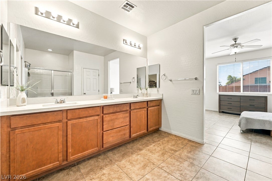 4209 Fairywren Drive, North Las Vegas, NV 89031 An expansive double vanity with warm wood cabinetry anchors this tiled primary bathroom suite.