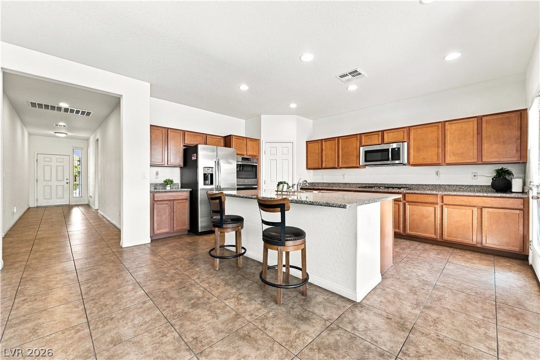 4209 Fairywren Drive, North Las Vegas, NV 89031 An open kitchen layout features rich wood cabinetry, granite countertops, and tile flooring throughout.