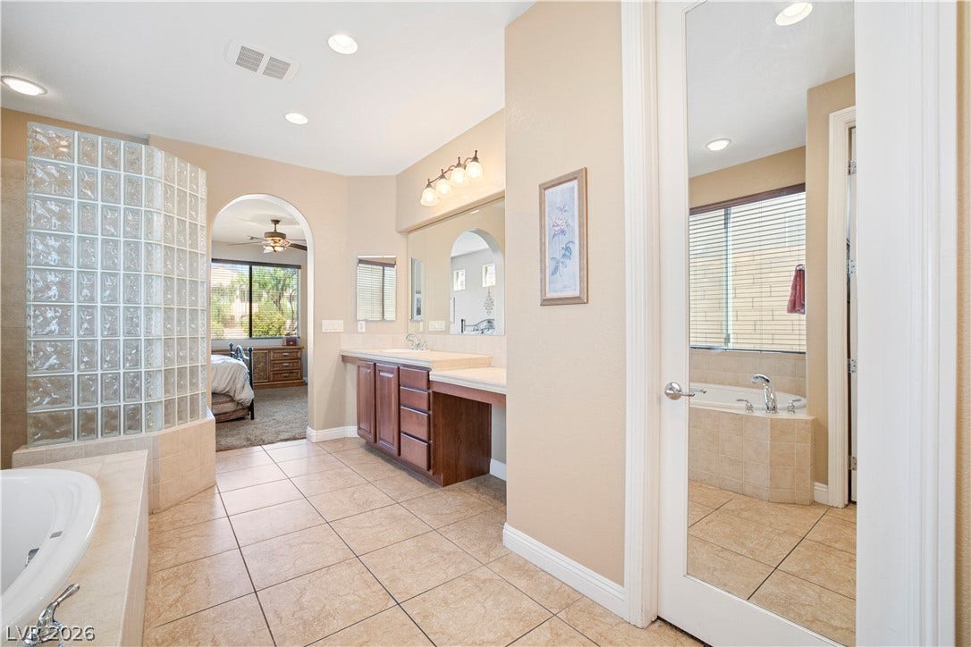 926 Loma Bonita Place, Las Vegas, NV 89138 Tiled flooring, dual vanities, and a glass-block shower enclosure define this main bathroom space.