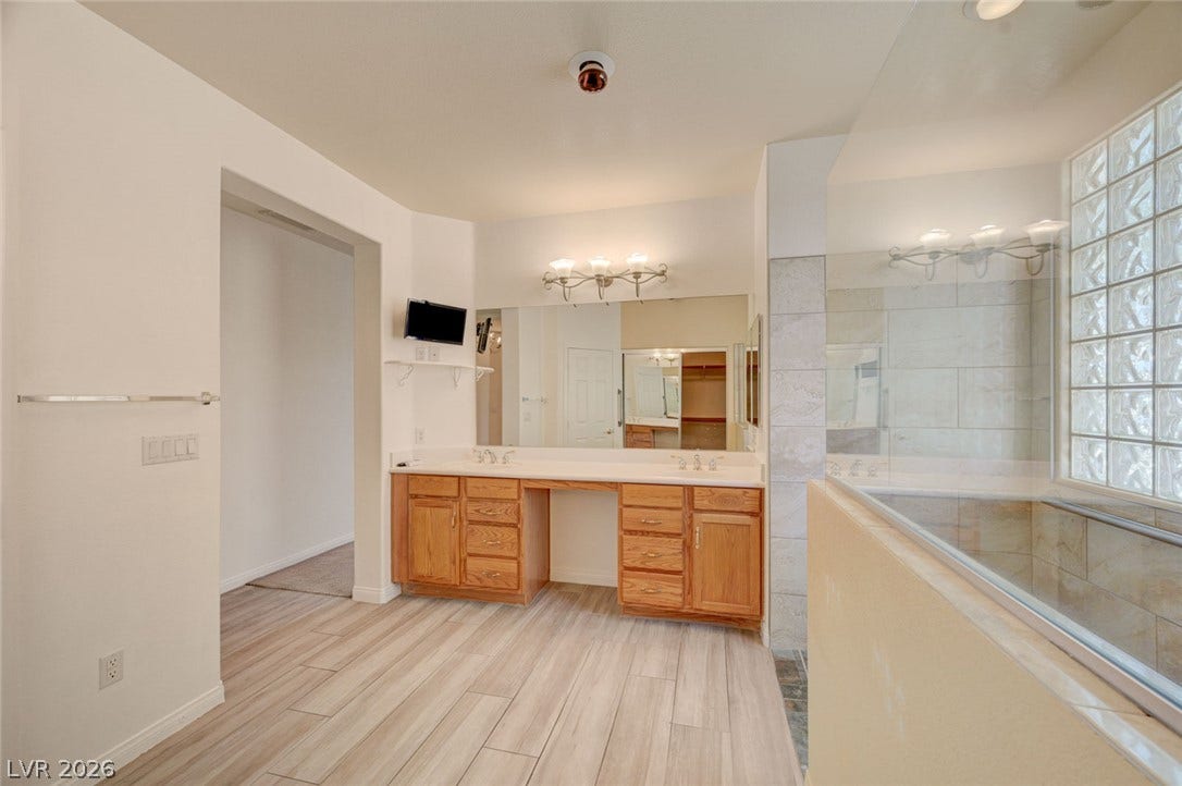 849 Ashford Way, Henderson, NV 89015 A generously sized primary bathroom features dual vanities and a glass-enclosed shower with a block glass window.