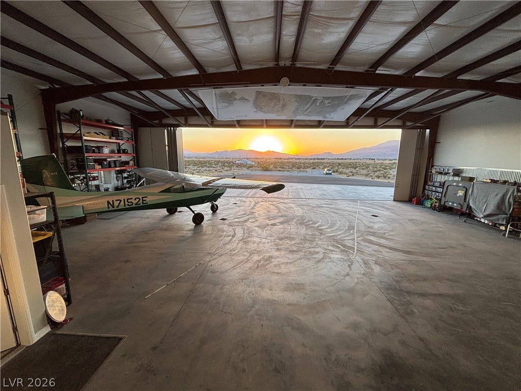 An expansive private airplane hangar features concrete flooring and mountain sunset views.