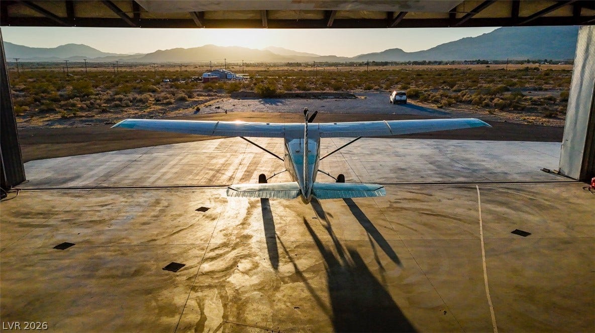 Dramatic mountain vistas frame the wide-open runway visible directly from the spacious hangar.