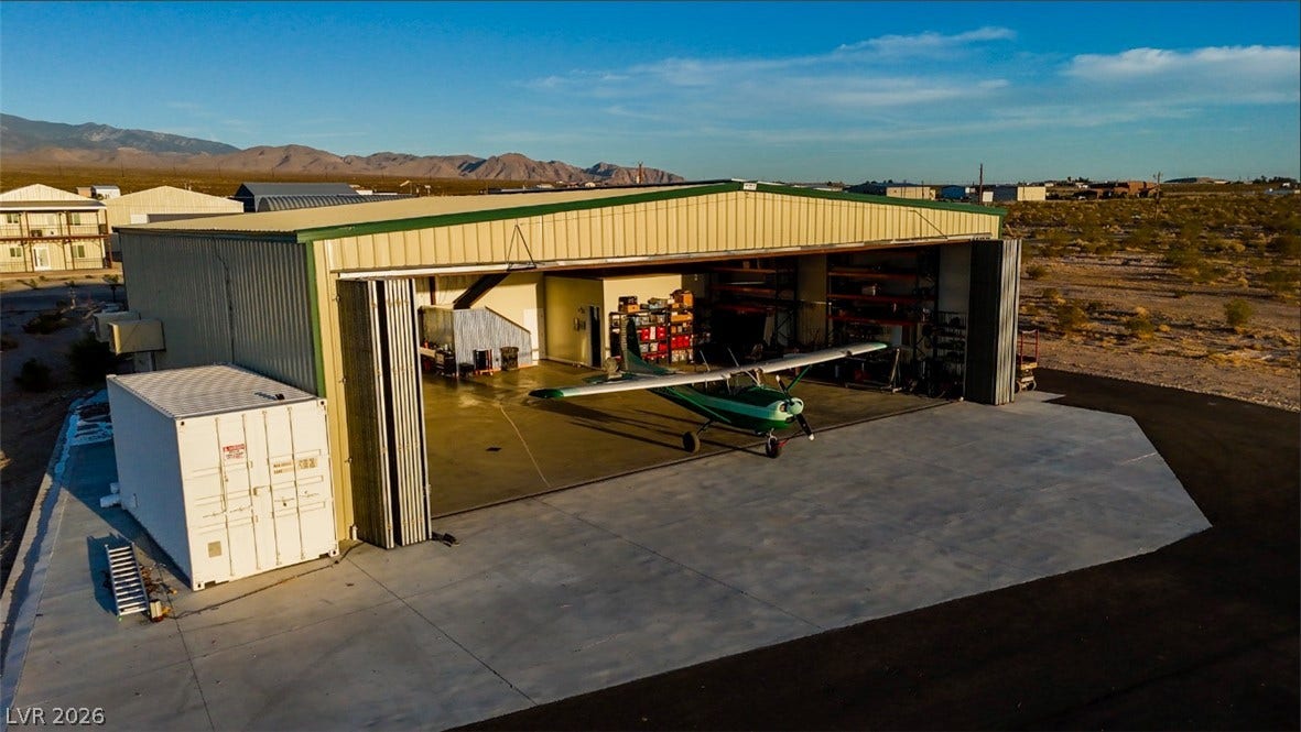 An expansive private airplane hangar stands ready for aircraft storage against a desert mountain backdrop.