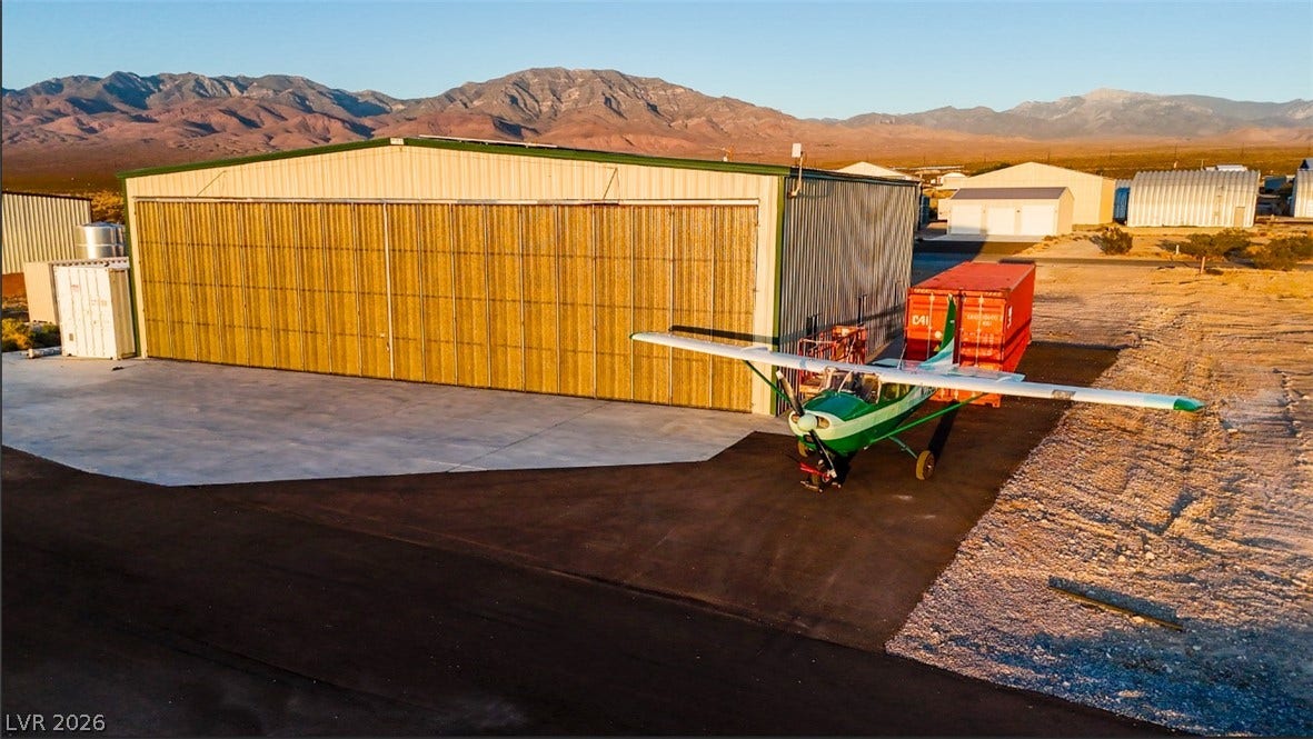 A spacious airplane hangar sits beneath a vast desert sky and striking mountain peaks.