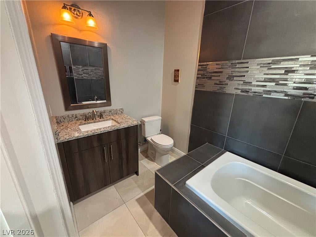 A deep soaking tub sits adjacent to a modern vanity with granite counters.
