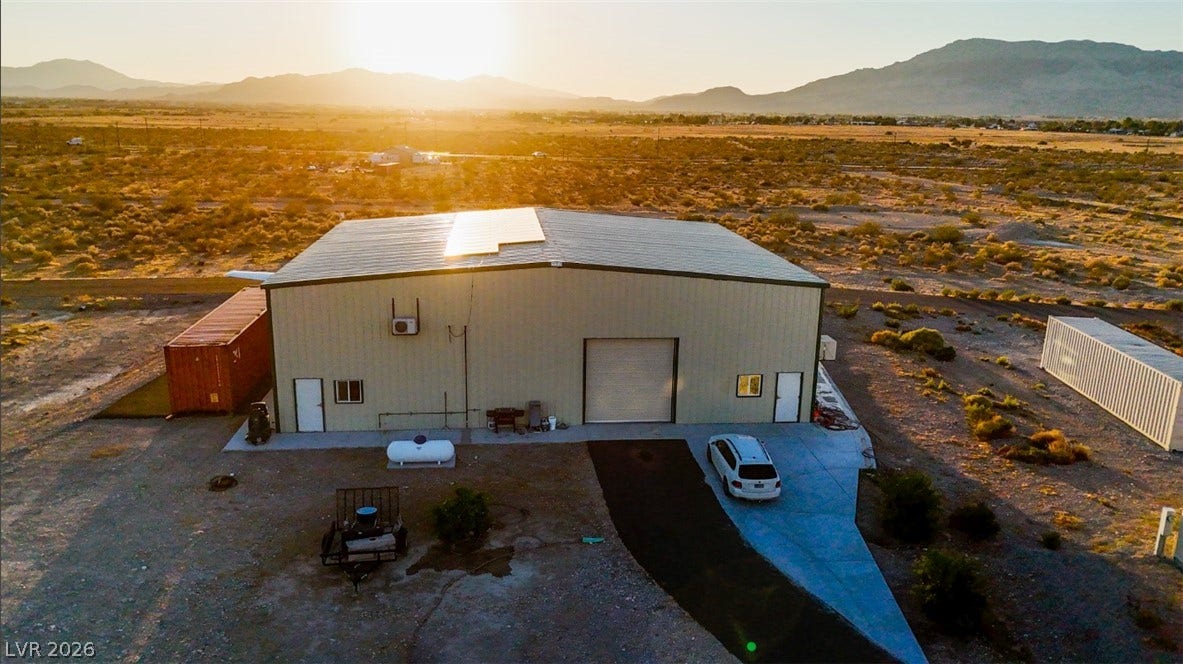 A spacious metal workshop sits under wide desert skies framed by distant mountain ranges.