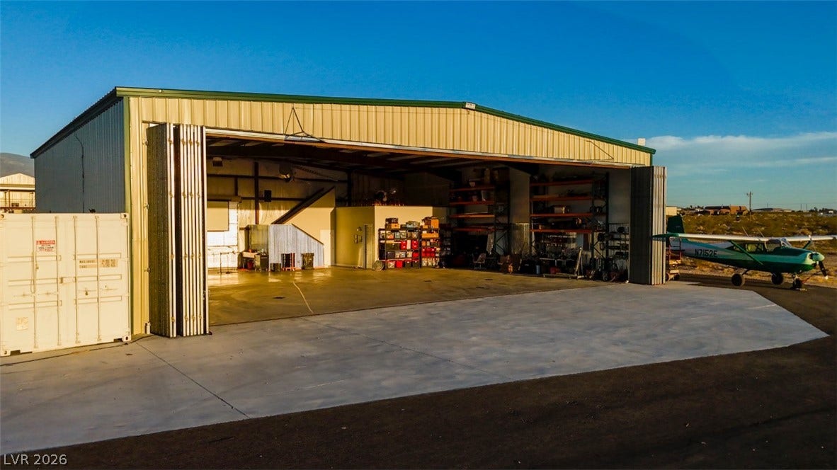 An expansive private airplane hangar features a massive bi-fold door and durable concrete flooring.
