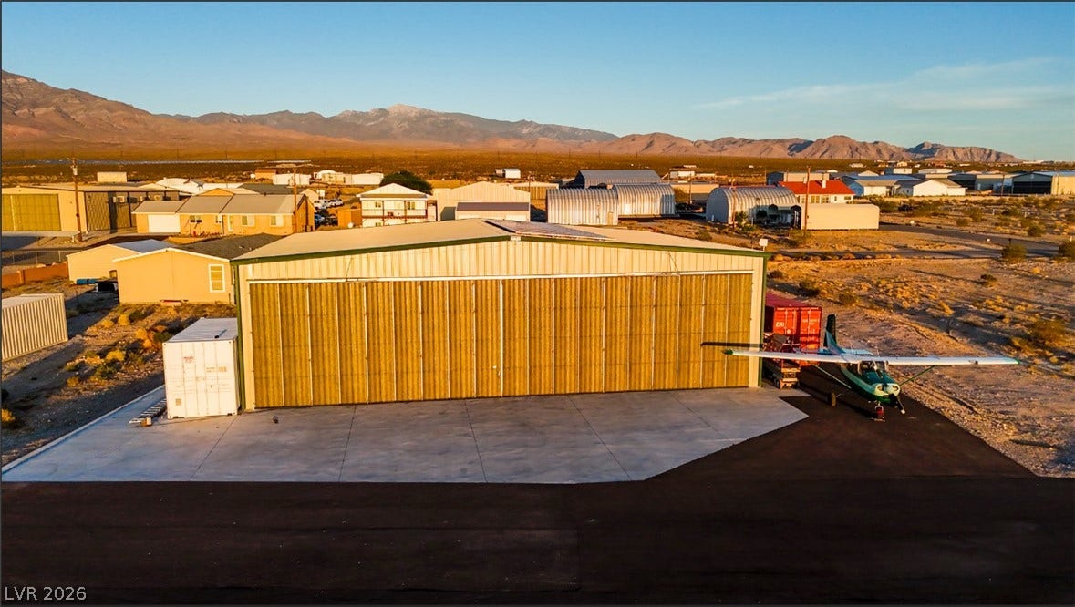 A spacious aircraft hangar rests on a concrete pad set against a desert mountain backdrop.