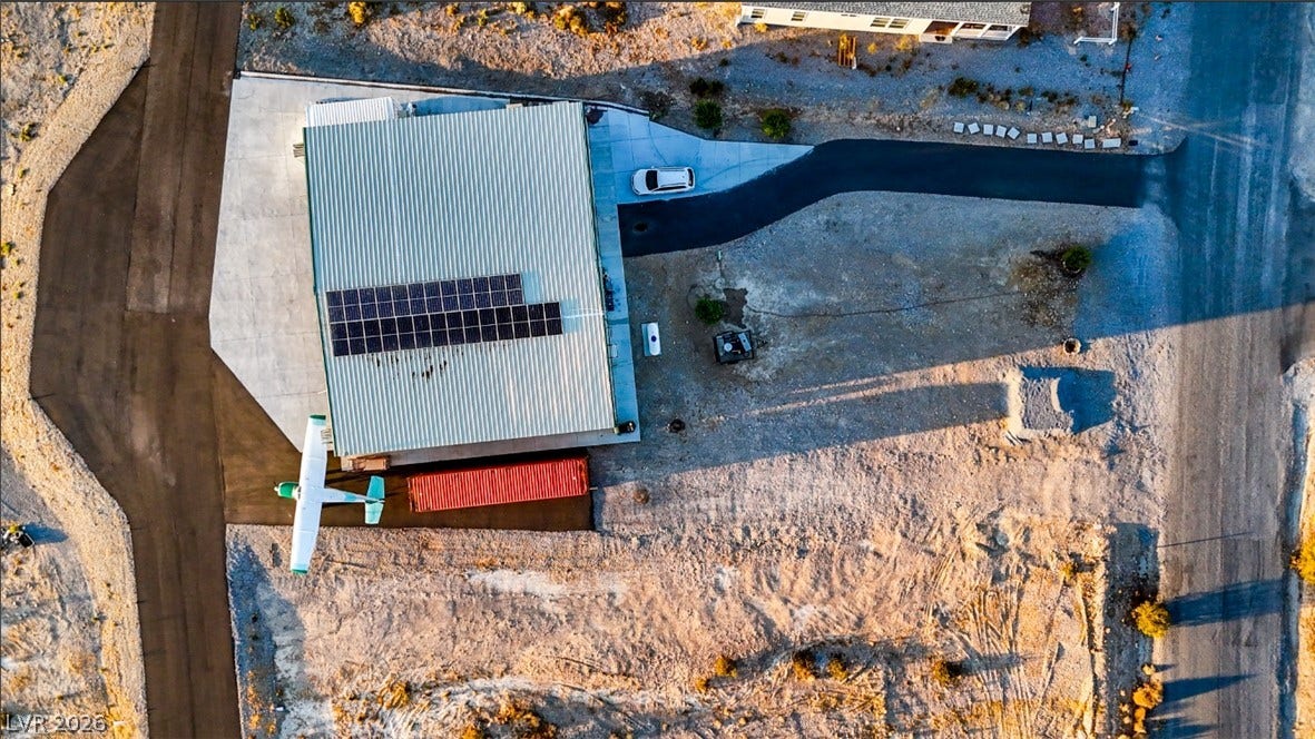 An aerial view showcases a metal-roofed hangar property complete with solar panels and taxiway access.