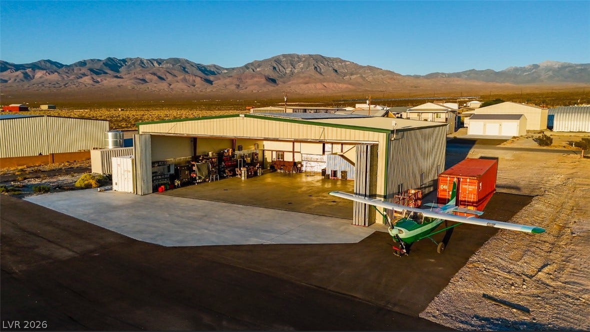 An expansive private airplane hangar features a concrete apron set against majestic mountain backdrops.