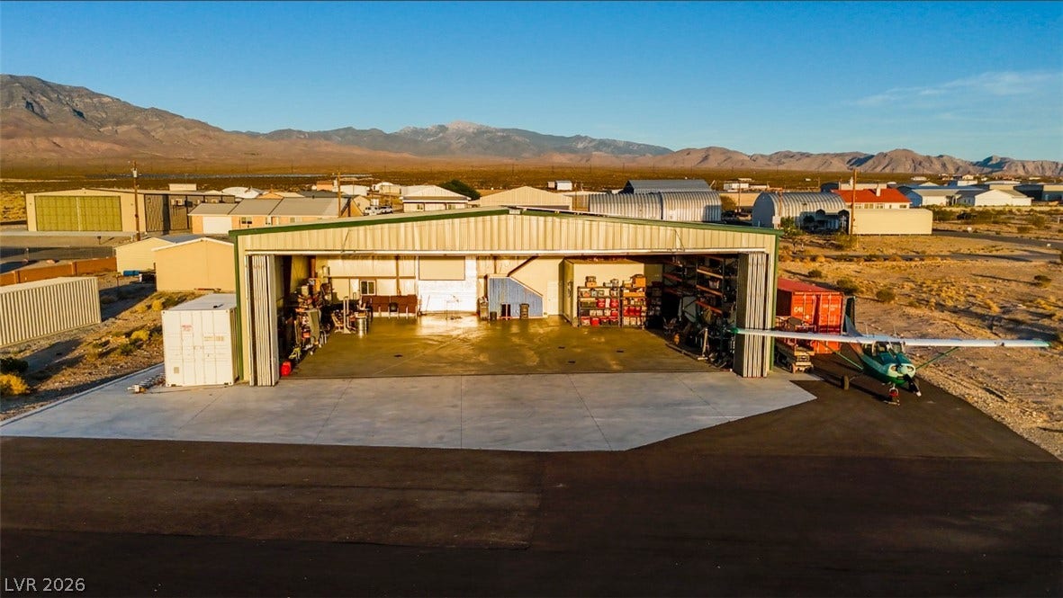 An expansive airplane hangar with a concrete apron sits against a dramatic mountain backdrop.