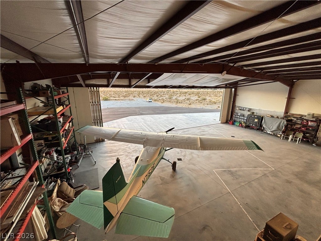 A spacious aircraft hangar features steel ceiling framing, concrete flooring, and a large folding door.